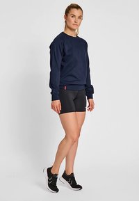 Marinblå sweatshirt med ribbade muddar och fåll, kombinerad med svarta träningsshorts och svarta sneakers med vita detaljer.