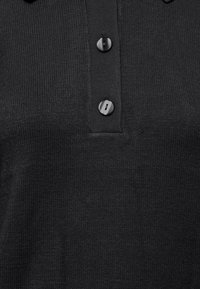 Juodas megztas polo marškinėliai su apykakle, trimis sagomis priekyje ir minkšta tekstūra. Audinys yra lengvas su briaunuota detalizacija.