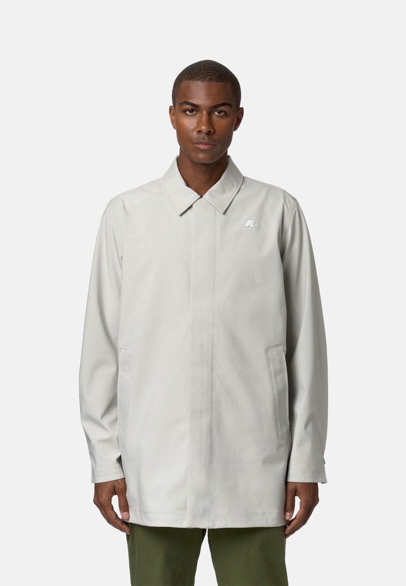 Cappotto impermeabile grigio chiaro con colletto a punta, due tasche laterali e un piccolo logo sul petto; texture liscia e vestibilità su misura.