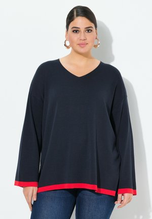 Námořnický pletený top s dlouhým rukávem a V-výstřihem, červený lem. Volný střih a měkká textura. V kombinaci s modrými džíny pro ležérní vzhled.