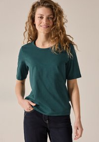 Teal krátký rukáv tričko vyrobené z měkké, lehké látky s kulatým výstřihem a mírným elastanem, spárované s tmavými džíny.