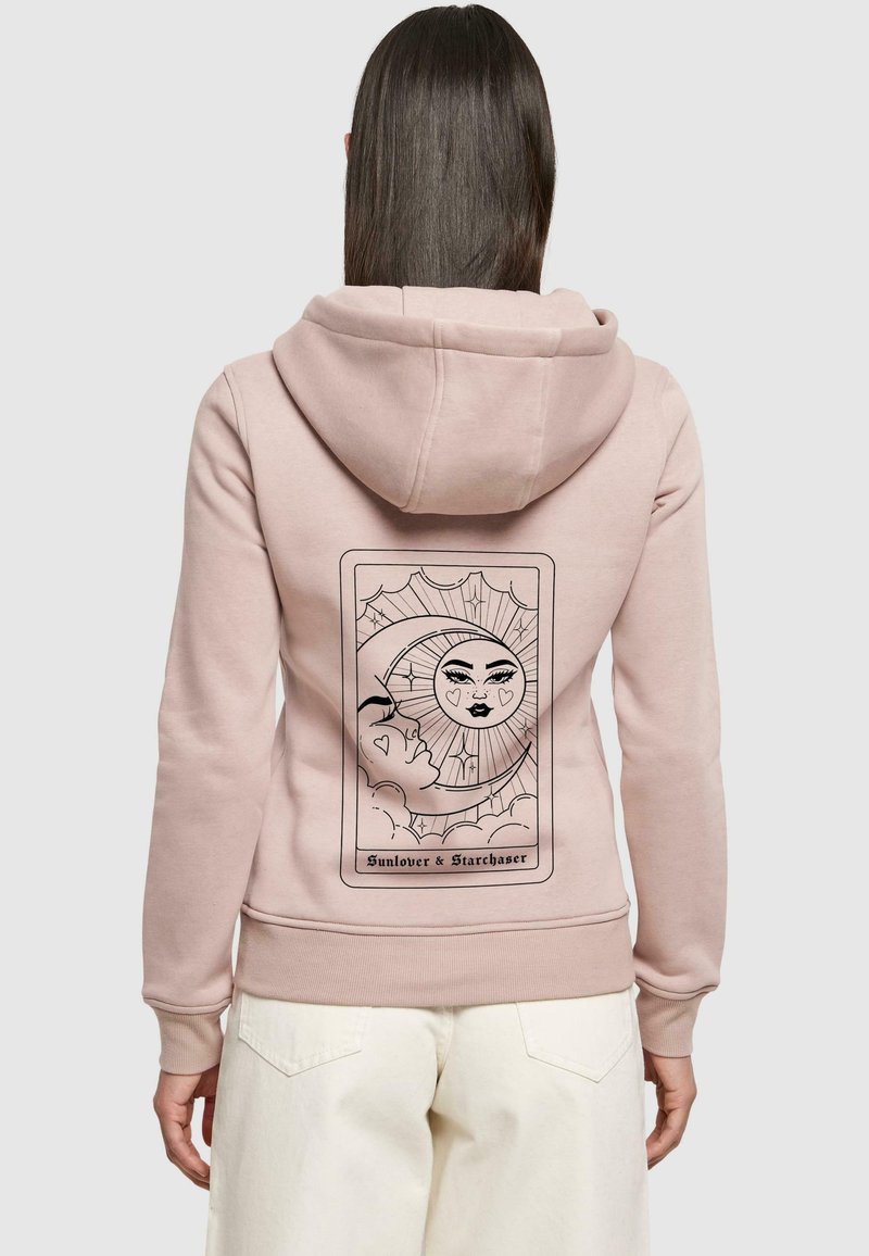 Ljusrosa hoodie med mjuk textur, med en grafisk design av en sol och måne på baksidan, inramad av dekorativa element.