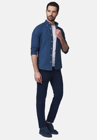 Granatowa koszula na guziki noszona na białym T-shircie, w zestawieniu z ciemnoniebieskimi spodniami slim-fit oraz dopasowanymi zamszowymi sneakersami. Gładka faktura materiału.