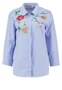 Niebieska, w paski, zapinana koszula z długim rękawem, z haftami przedstawiającymi kwiaty i ptaki z przodu. Materiał ma gładką fakturę.