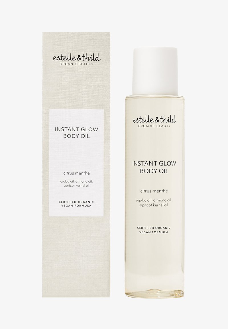 Gjennomsiktig glassflaske med hvit kork, merket "Instant Glow Body Oil." Akkompagnert av en beige boks med minimalistisk tekst.