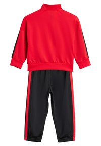 Chándal deportivo rojo con cuello alto, mangas largas y acentos negros a lo largo de los lados del pantalón. Hecho de una tela suave y elástica.