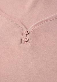 Gros plan sur un tissu rose avec deux petits boutons assortis et des coutures visibles le long d'un col arrondi.