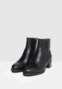 Schwarze Leder-Stiefeletten mit einem seitlichen Reißverschluss, einer viereckigen Zehenpartie, einem niedrigen Blockabsatz und einem dekorativen Riemen mit einem metallischen Akzent.