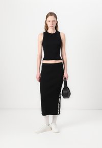 Fekete bordás kötött crop top és hozzá illő közép hosszúságú szoknya oldalsó szövegrészlettel. Fehér tornacipővel és egy kis fekete táskával párosítva.