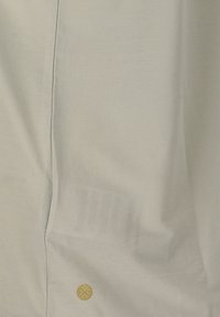 Tessuto grigio chiaro con una texture liscia. Presenta cuciture sottili e un piccolo emblema circolare dorato vicino all'angolo in basso a destra.