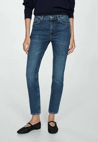 Dark blue denim jeans with a slim fit, five pockets, and a classic button closure. Paired with black flats and a navy sweater.