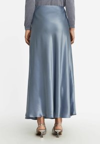 Jupe maxi en satin de couleur bleu clair, présentant une texture lisse et un design fluide. L'ourlet est arrondi, avec une légère brillance. Associée à des chaussures à talons argentées.