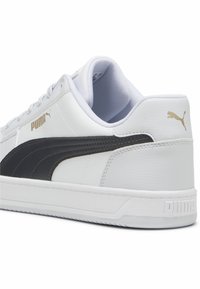 Bijela tenisica s crnim kožnim detaljima, s teksturiranom površinom, okruglim vrhom i podstavljenim ovratnikom oko gležnja. Zlatni Puma logo sa strane.