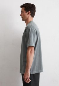 T-shirt en coton gris avec une coupe décontractée, manches courtes, fentes sur les côtés et encolure ronde. Texture lisse, présentant des détails de design minimalistes.