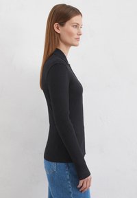 Schwarzes, geripptes Langarmtop mit slim Fit, Knopfleiste und klassischem Kragen; kombiniert mit hellblauen Denim-Jeans. Textur sichtbar.