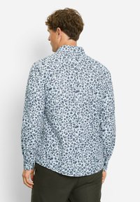 Himmelblaues Langarmhemd mit floralem Muster in Marineblau, Rot und Weiß. Button-Down-Kragen, abgerundeter Saum und strukturierter Stoff.