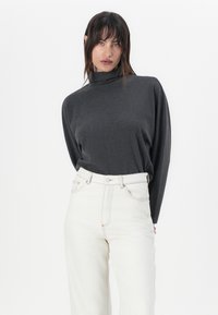 Grå høyhalset genser med avslappet passform. Kombinert med høyhalsede, off-white jeans med kontrastsøm og knappelukking.
