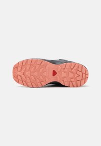 Suela de zapato deportivo negro con un patrón de textura en rosa, diseñada para ofrecer tracción y estabilidad en varios terrenos.