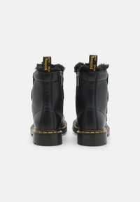 Černé kotníkové boty s texturovaným koženým povrchem, huňatým podšívkou, žlutým prošitím a poutkem na patě. Zipové zapínání po obou stranách.