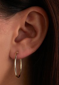Boucle d'oreille en or présentée en gros plan, mettant en avant une surface lisse et brillante, une forme circulaire et un design fin reposant sur l'oreille.