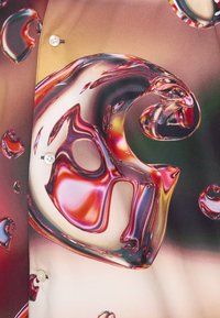 Chemise colorée présentant un motif de bulles tourbillonnantes brillant, avec des nuances de rouge et d'or, fabriquée en tissu doux, affichant un détail de bouton.