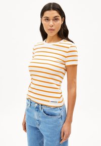 Witte t-shirt met korte mouwen en oranje horizontale strepen, een ronde halslijn en een label aan de zoom. Temidden van lichtblauwe denim jeans.