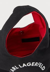 Fekete vászontáska piros szövetbéléssel, mágneses gombzárral, és a külső oldalán fehér "KARL LAGERFELD" felirattal.