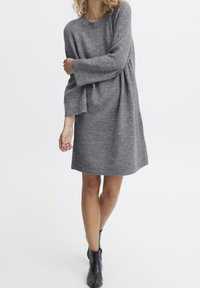 Robe en maille grise à la coupe décontractée, manches longues et texture douce. Associée à des bottines noires.