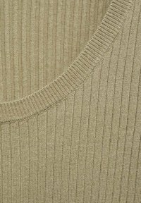 Tessuto a coste in un verde oliva tenue. Il collo è rotondo, evidenziando un motivo a maglia testurizzato con lievi variazioni.