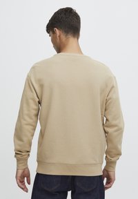 Hnědý crewneck svetr s dlouhými rukávy a ribbovanými manžetami, vyrobený z měkké tkaniny. Má jednoduchý design bez viditelných log nebo vzorů.