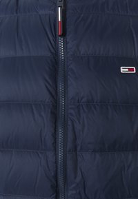 Chaqueta acolchada azul marino con cremallera central y parche logo rectangular pequeño en el lado izquierdo en colores blanco, rojo y azul marino.