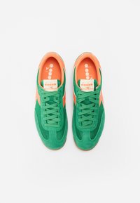 Grønne og oransje atletiske sko laget av semsket skinn og mesh-materiale. Funksjoner inkluderer snøring, gummisåler og diagonale sideakenter.