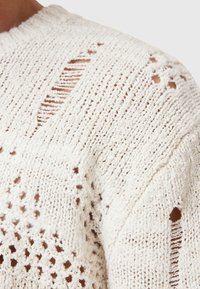Chunky knit sweater in cream color with openwork stitching. Features various textures and irregular openings throughout the fabric.
