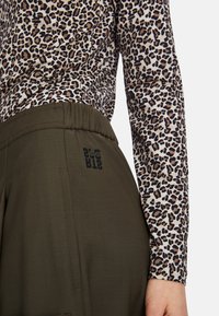 Brown leopard print long-sleeve top paired with olive green pants featuring an elastic waistband and a printed logo on the back pocket.