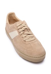 Beige suède sneaker met een gestructureerd oppervlak, ronde neus en dikke beige veters. Voorzien van een gladde, crèmekleurige side stripe en een rubberen zool.