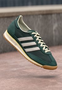 Green suede and mesh sneaker with three white stripes, tan rubber sole, cream laces, and a streamlined design. Lightweight and breathable.