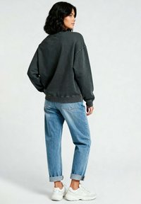 Felpa oversize grigia scuro con orlo a coste, abbinata a jeans azzurri risvoltati e sneakers bianche. Tessuto liscio e vestibilità rilassata.