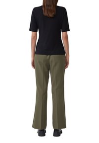 Un haut noir à manches courtes associé à un pantalon large vert olive, présentant une texture lisse et un devant plat, complété par des chaussures noires.