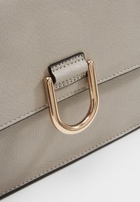 Šedá kožená kabelka s akcentem z kovového hardwaru ve zlatém odstínu a kontrastním černým prošíváním podél okrajů.