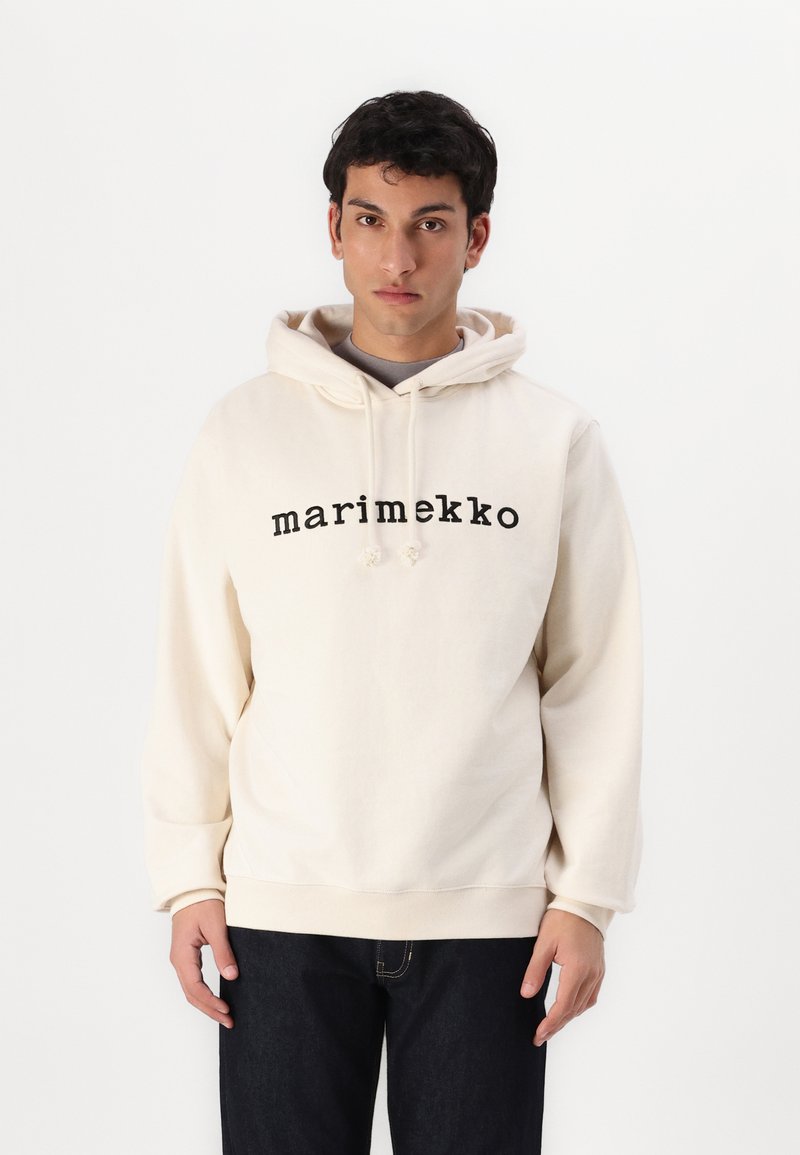 Krém színű kapucnis pulóver állítható zsinórral, az elején nyomott "marimekko" logóval, sötét farmernadrággal párosítva. Puha anyag, laza fit.