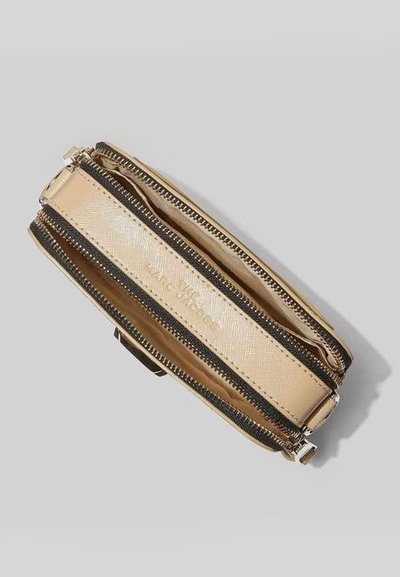 Borsa a tracolla in pelle beige con due cerniere nere a contrasto, texture liscia, design piatto e logo in rilievo dorato sul lato.