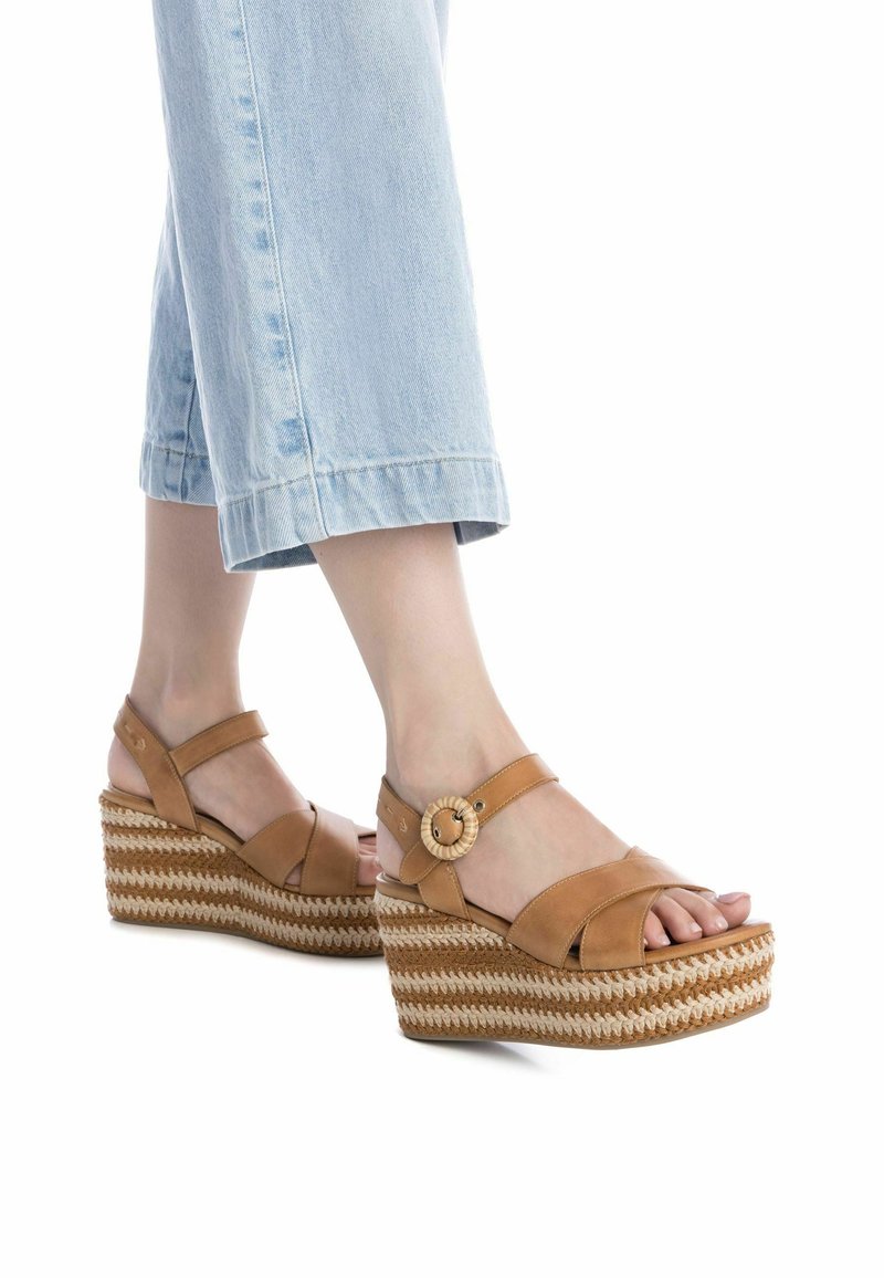 Sandali wedge in pelle marrone con fasce incrociate e un accentuazione in legno rotondo. La suola presenta un design intrecciato in paglia e un aspetto a strati.