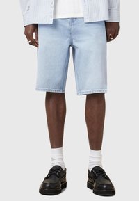 Shorts en denim bleu clair avec une coupe droite, cinq poches et des ourlets cousus. Portés avec des chaussettes blanches et des chaussures noires.