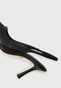 Chaussure à talon haut en cuir noir avec un design à bout ouvert, un talon fin et des détails de brides croisées avec une finition lisse.