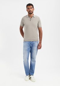 Lichtgrijze polo met korte mouwen en drie knopen, gedragen met lichtblauwe rechte spijkerbroeken en witte sneakers. Eenvoudig, casual ontwerp.