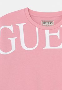 Pink cotton sweatshirt featuring a large white "GUESS" logo across the front and a ribbed crew neckline. Smooth texture, casual style.