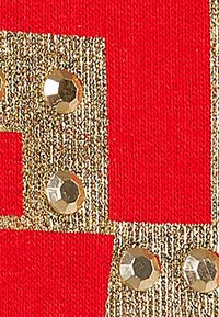 Il tessuto rosso presenta motivi geometrici dorati con paillettes lucide e riflettenti incorporate nel design, aggiungendo texture e dettaglio.