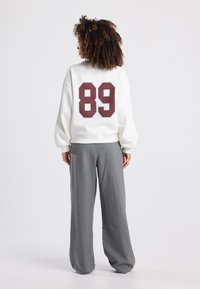 White sweatshirt with maroon "89" print on the back, paired with gray wide-leg trousers. The materials appear soft with a relaxed fit.