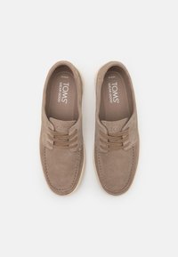 Tan suede batai sugiu struktūra, turintys laido dizainą, siuvinėtus akcentus ir lengvą guminį padu. TOMS prekės ženklas matomas viduje.