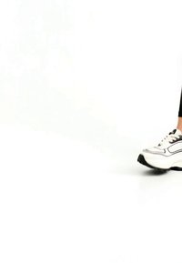 Pravá noha v černých legínách a bílé tenisce s černou podrážkou na bílém pozadí, polokrok vpřed.